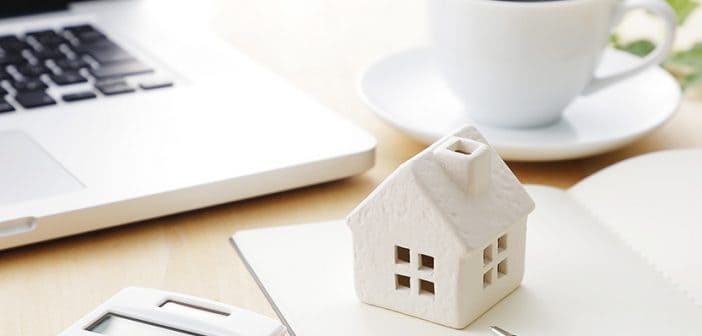 wooden model of house on desk with coffee cup, calculator, laptop