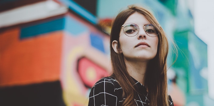 woman in plaid shirt with glasses standing in front of colorfully painted building