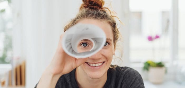 Young woman playing I spy with the camera looking through a rolled cylinder of paper with one eye and a happy smile