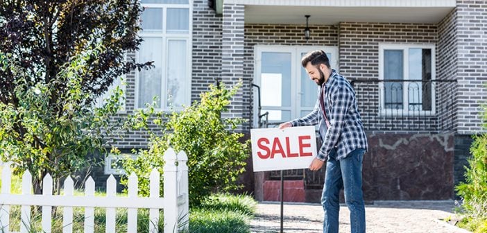 young man placing sale sign in front of his house