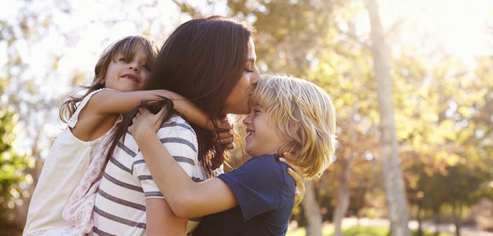 Mother Carrying Son And Daughter As They Play In Park