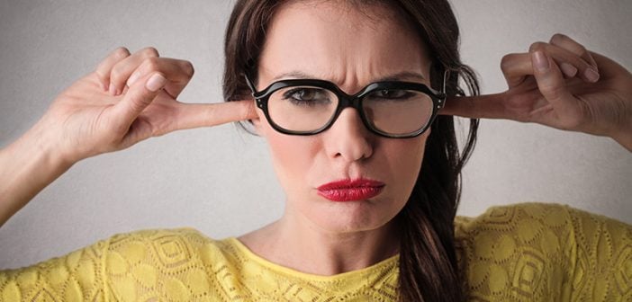 closeup of woman in yellow shirt plugging ears with fingers wearing red lipstick and glasses