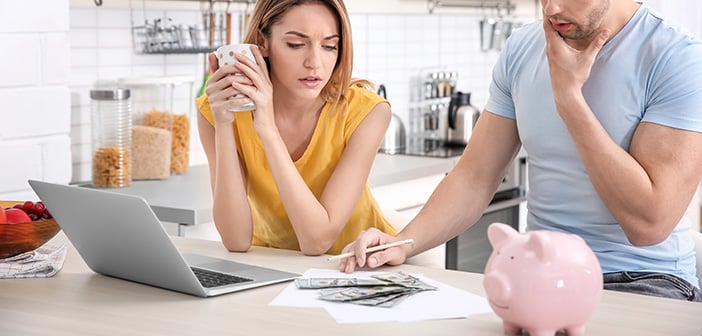 young couple looking over financials in kitchen on computer and printed papers with piggy bank and money in view