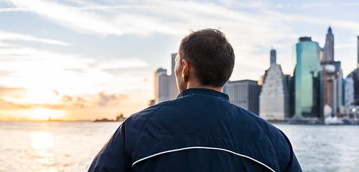 man looking out over river at cityscape and sunset