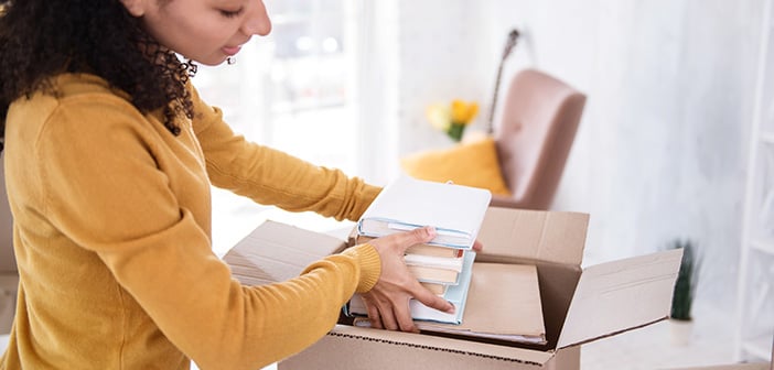 Girl packing books into a box in a brightly lit living room