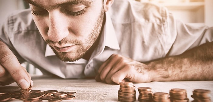 bearded man wearing white shirt hovered over pile of pennies counting them