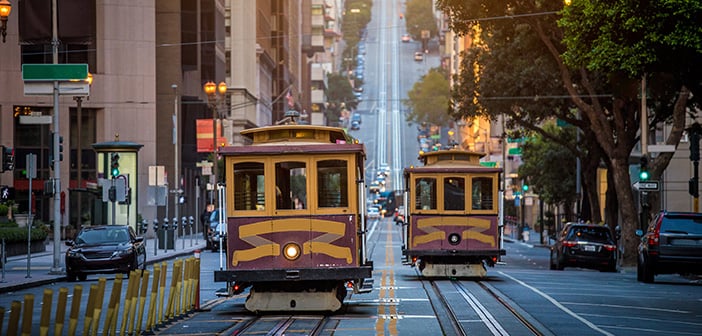 Classic view of historic traditional Cable Cars riding on famous California Street in beautiful early morning light at sunrise during summer in San Francisco