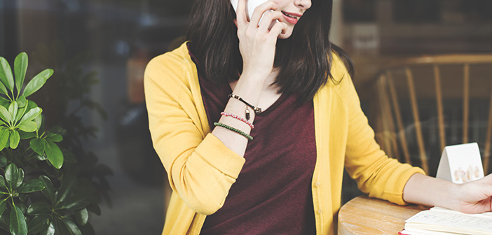 woman in maroon shirt and yellow sweater talking on a cell phone while going over notes on a notepad