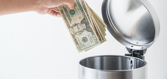 closeup of hand holding a stack of cash and preparing to throw it in a trash can