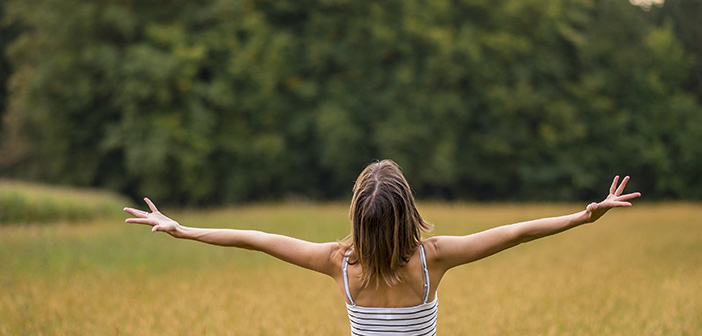 Woman with her back to the camera standing in autumn meadow with her arms spread widely as she enjoys the beauty of life and nature.