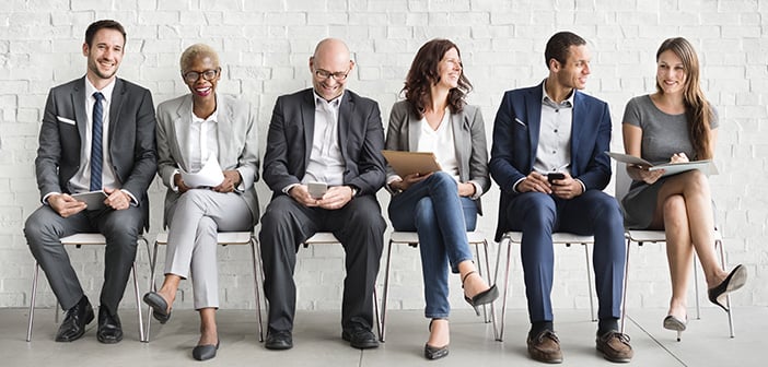 Group of diverse people are seated and waiting for a job interview in a waiting room with white walls and light colored floor