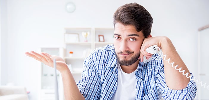 frustrated young man with one hand up signifying confusion and phone in other hand