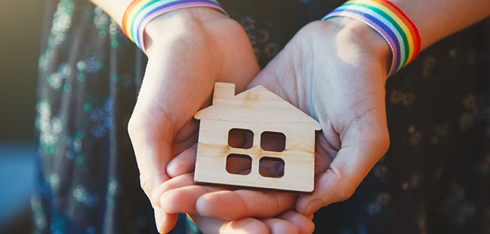 young female hands with LGBT rainbow ribbon wristbands holding craft wooden house