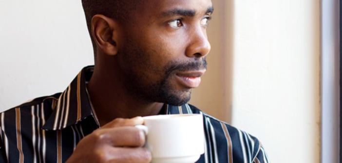 african american man drinking coffee looking out a window