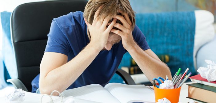 Frustrated student behind the desk keeping hands on face