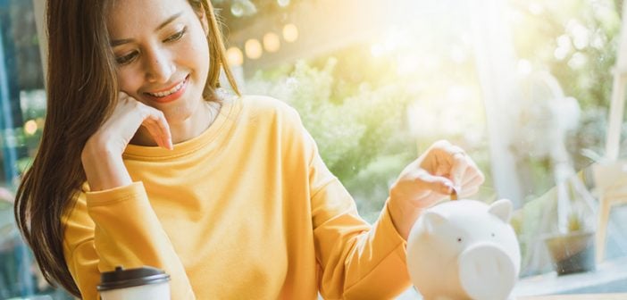 Asian woman saving money and dropping coin to piggy