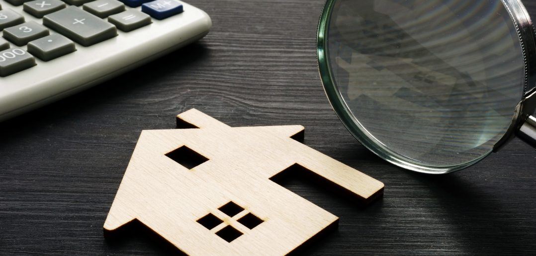 Property assessment. Wooden house with magnifier and calculator.