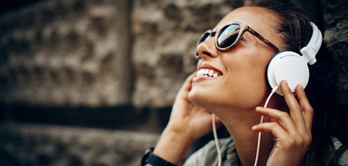 smiling dark haired girl listening to white headphones and smiling sitting outside in urban setting