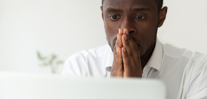 Thoughtful hopeful African American employee looking at computer laptop screen, waiting hoping, person holding hands in praying position, expecting trouble solution, positive result, close up portrait