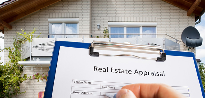 Close-up Of Person Hand Filling Real Estate Appraisal Document In Front Of House