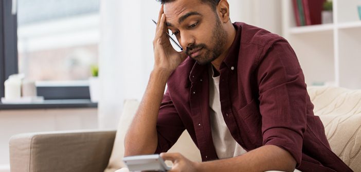 business, accounting, finances and people concept - confused man with calculator at home