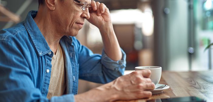 Close up side on portrait of smiling aged male in glasses sitting with cup of coffee in cafe alone