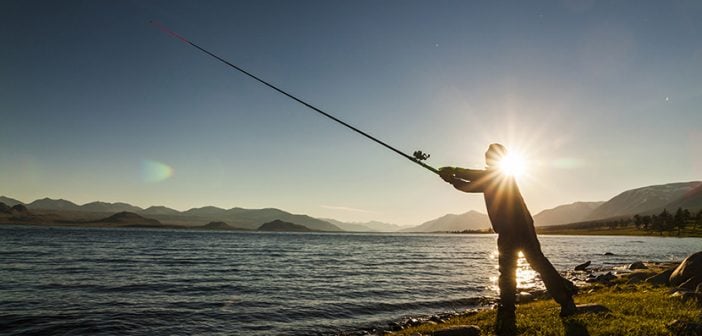 Silhouette of a fisherman at sunset. Fishing on mountain lake