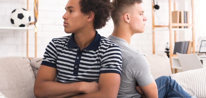 two young men sitting back to back with arms folded in frustration in a living room setting