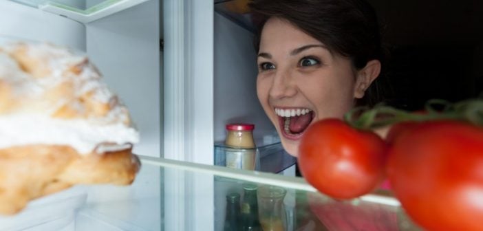 woman looking in refrigerator with menacing grin at dessert