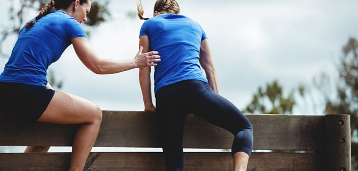 Female trainer assisting woman to climb a wooden wall