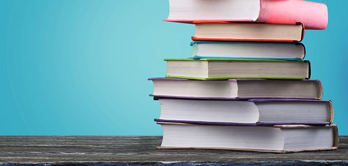 stack of colorfully bound books against turquoise background on dark wood table