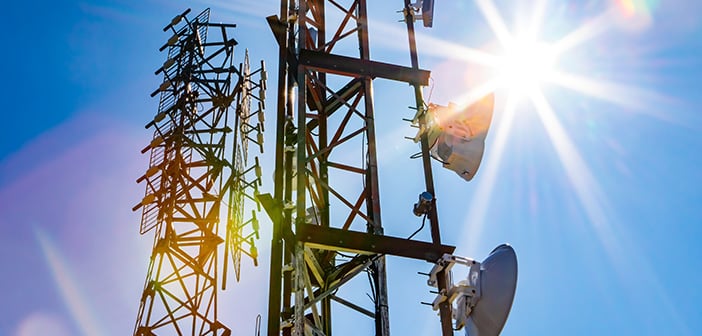 Bright sun shine over two cell site towers, radio and GPS transmitter and receiver, associated with electromagnetic pollution, with vibrant lens flare