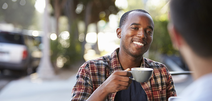 Two adult male friends sit talking over coffee outside cafe