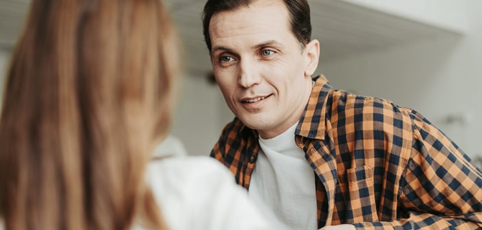 Calm middle aged man in checkered shirt sitting and looking attentively at his daughter while talking to her