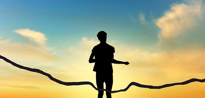 silhouette of human figure running through ribbon at finish line set against vividly colored sunset and foothill backdrop