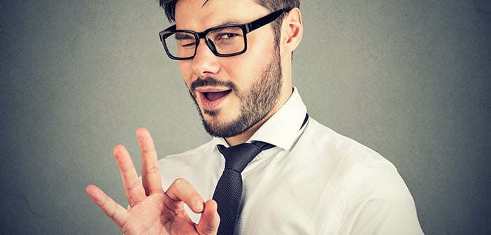 Young bearded man in glasses showing OK gesture and blinking at camera with overconfidence