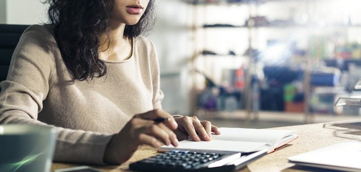 Portrait of a concentrated Asian accountant at her workplace using her calculator. Concept of accounting in business.