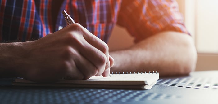 male hand writing in notebook with pen