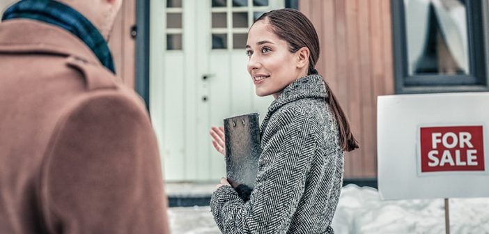 Smiling realtor greeting her customers outside the house for sale in winter with snow on ground