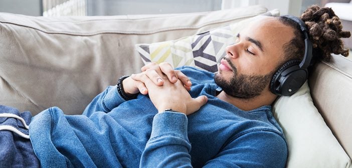 african american young man lying on couch listening to headphones