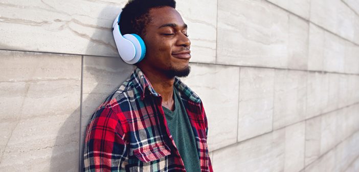 Portrait happy smiling african man in wireless headphones enjoying listening to music on city street over gray wall background