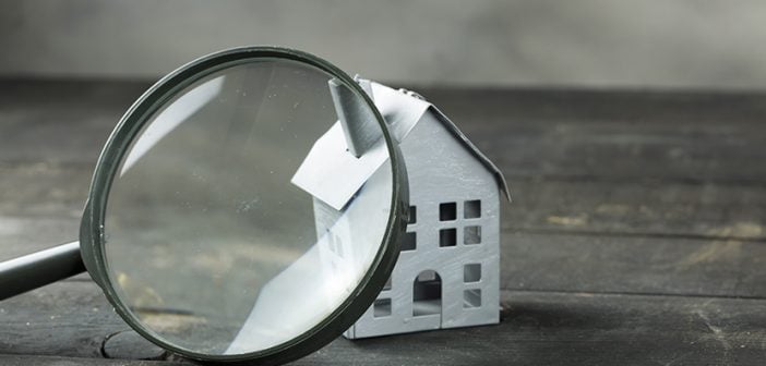 small white model of house on dark-stained wooden surface with magnifying glass enlarging portion of home