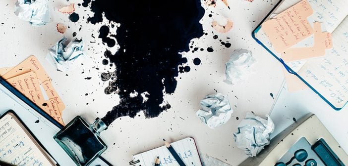 Writer workplace with spilled ink, stationery and a typewriter. Crumpled paper balls with pencils on a white wooden background, creative writing concept.