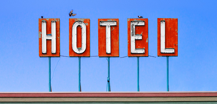 Red hotel sign on top of a dirty old motel isolated on blue sky background with birds