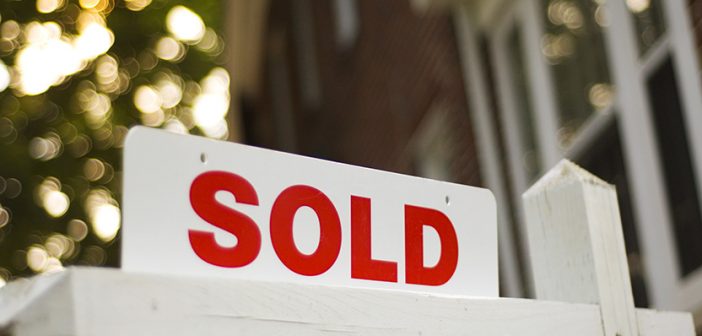 Real Estate "sold" sign with red brick building and trees blurry in the background