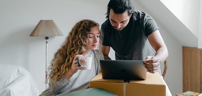 couple in living room amid moving boxes looking at laptop together