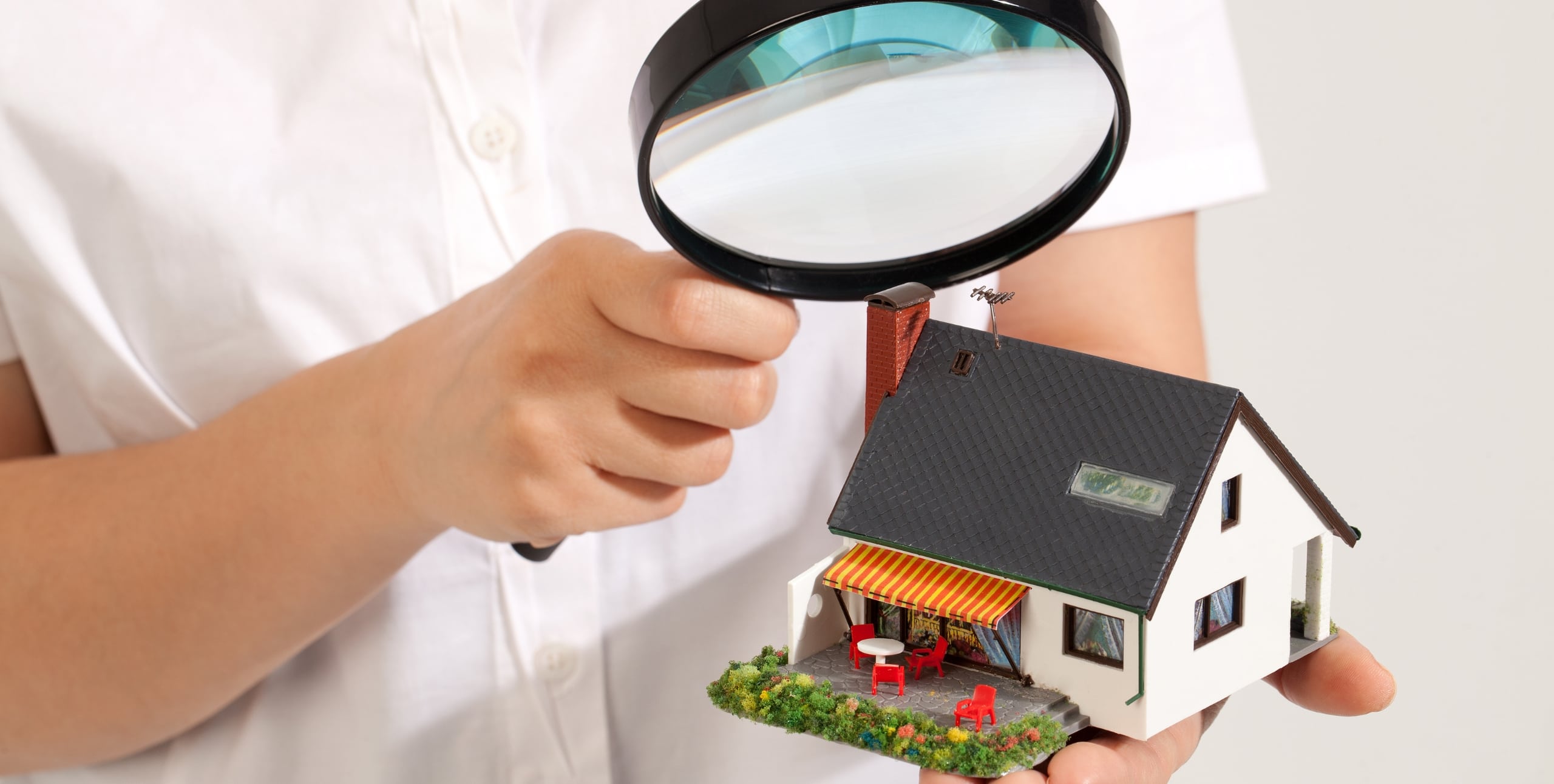 person holding magnifying glass to home