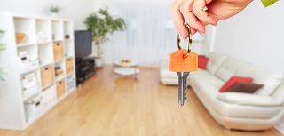 person holding house key with living room in background