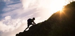 silhouette of man wearing backpack climbing uphill in sunshine