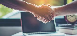 close up of two men shaking hands one light skinned one dark skinned laptop in background